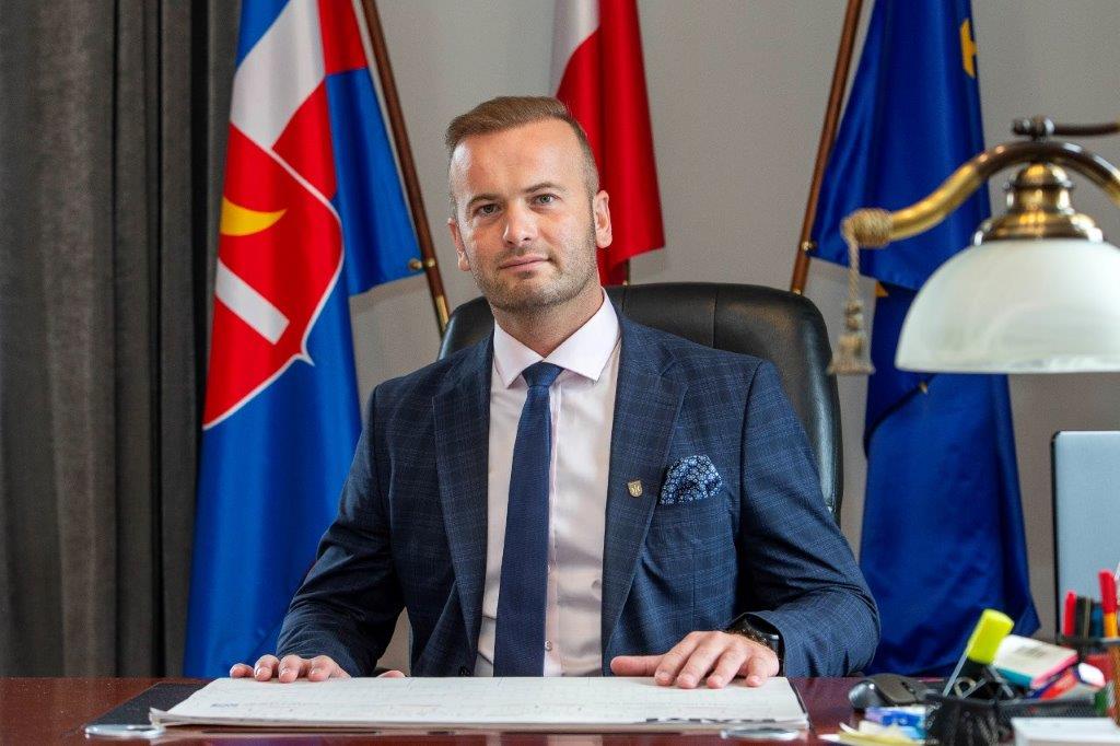 Burmistrz Świecia Krzysztof Kułakowski za biurkiem, w tle flaga Polski, UE i Gminy Świecie