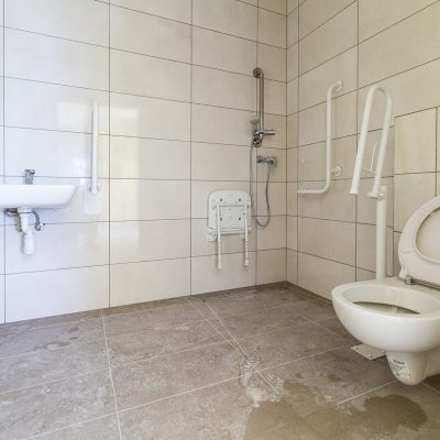 łazienka wyłożona kafelkami w domu z mieszkaniami chronionymi, na pierwszym planie toaleta w oddali umywalka
