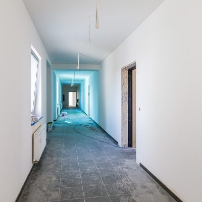 korytarz w domu z mieszkaniami chronionymi, po środku korytarza rośniagniety przewód elektryczny, z sufitu zwisają przewody elektryczne,