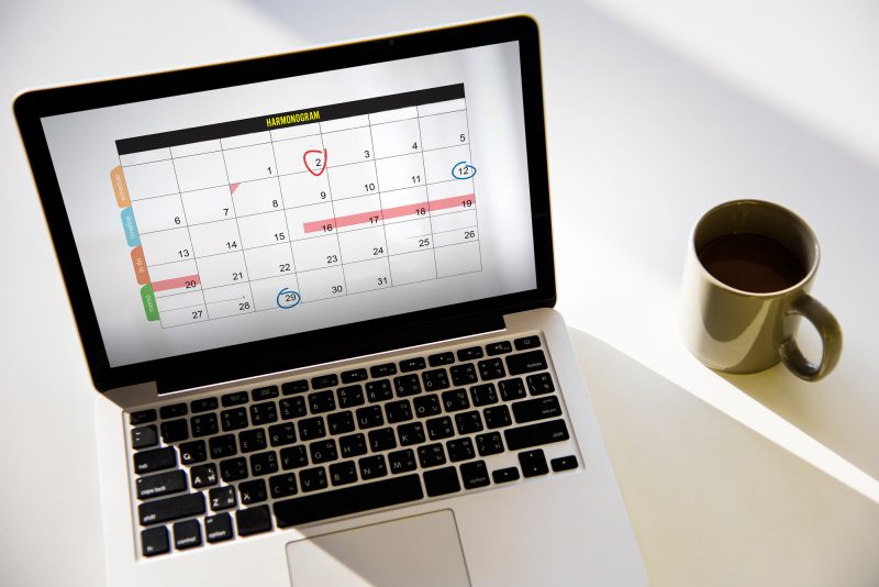 komputer z wyswietlonym kalendarzem, obok kubek z kawą